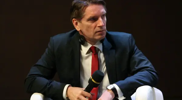Tomasz Lis w garniturze i czerwonym krawacie, z mikrofonem w dłoni. Mówi o swojej chorobie.