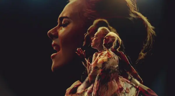 Adele śpiewa "Send My Love" w wielokrotnej ekspozycji, jej twarz i postać w sukni rozmywają się w mroku.
