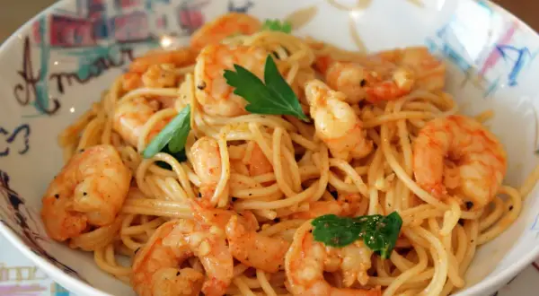 Un plat de pâtes aux crevettes, garni de persil frais, servi dans un bol décoré. Un délice pour les yeux et les papilles.