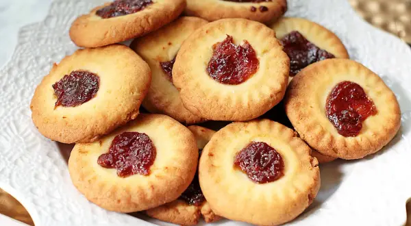 Stos ciastek bez jajek z dżemem w środku, ułożonych na białej paterze. Idealne na podwieczorek.