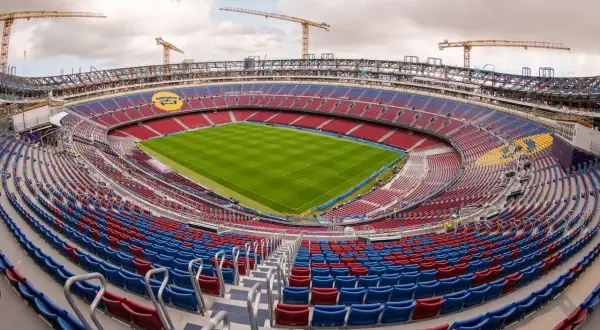 Widok na budowę nowego Camp Nou. Krany budowlane górują nad trybunami stadionu w kolorach czerwonym i niebieskim, z zieloną murawą boiska.