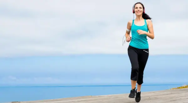Mujer sonriente corriendo junto al mar, disfrutando de ejercicios para trabajar la autoestima y sentirse bien.