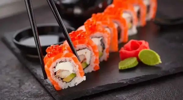 Chopsticks podnoszą kawałek sushi z łososiem i ikrą. Czy sushi jest lekkostrawne? Zależy od składników, ale to danie wygląda apetycznie.