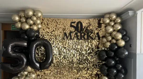 Złote i czarne balony otaczają błyszczące tło z napisem "50 lat Marka".