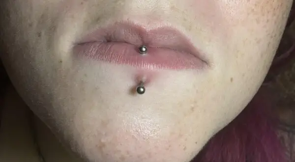 Labret co to? Kolczyk w wardze i pod nią, ozdobiony metalowymi kulkami. Skóra z piegami.