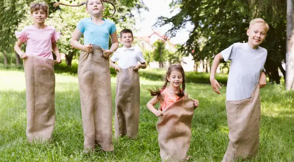 Niños compiten en carreras de sacos en un día soleado, disfrutando en familia de juegos al aire libre.