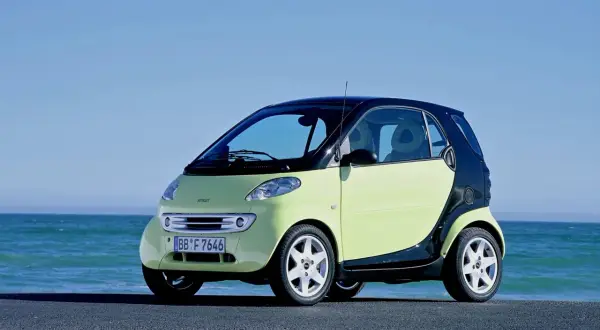 Jasnozielony smart fortwo 450 z czarnym dachem i czarnymi panelami bocznymi stoi nad błękitnym morzem.