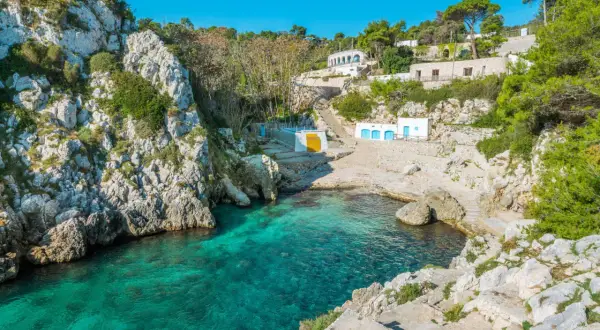 Baia incantevole con acque cristalline, rocce bianche e case bianche con porte blu. Il meglio della Puglia.