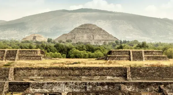 Majestätische Maya-Ruinen erheben sich vor einer sanften Bergkulisse. Alte Steinstrukturen und Pyramiden zeugen von einer vergangenen Zivilisation.
