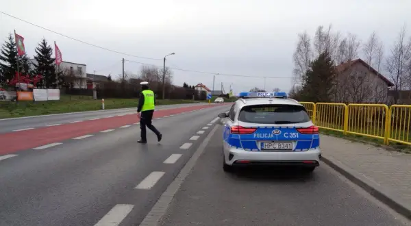 Policjant w kamizelce odblaskowej kieruje ruchem obok radiowozu. Może to być kontrola drogowa lub reakcja na wykroczenie 97 kw.