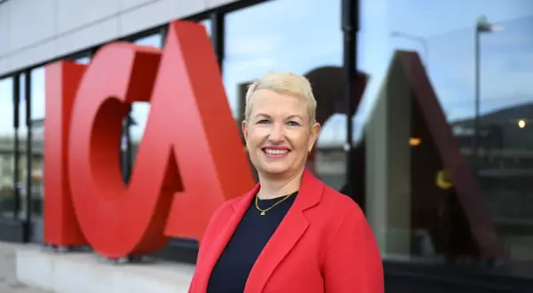 En leende kvinna i röd kavaj framför stora röda bokstäver som bildar ICA. Hon är ICA:s VD.