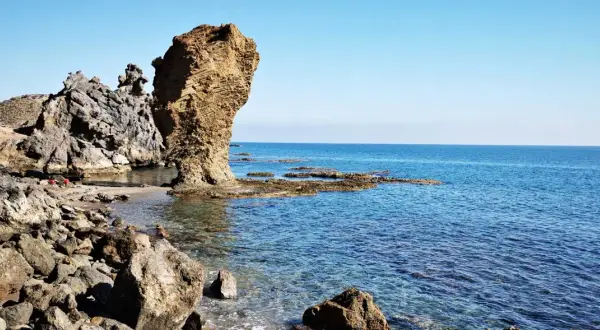 Rocas erosionadas y mar azul en la playa El Sombrerico. Una formación rocosa alta se alza como un guardián.