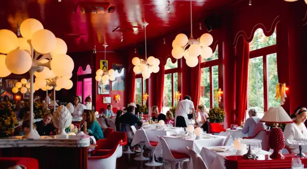 Ein lebhaftes **Cafe Berlin Mitte** mit roten Wänden, auffälligen Kugelleuchten und Gästen, die an weiß gedeckten Tischen sitzen.