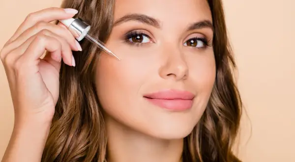 Kobieta aplikuje serum z pipetki na policzek. Dowiedz się, jak stosować retinol dla pięknej cery.