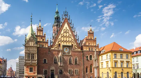 Stary Rynek we Wrocławiu tętni życiem. Wspaniały Ratusz z zegarem astronomicznym dominuje nad placem, gdzie spacerują ludzie.