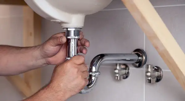 Hände schrauben am Siphon unter dem Waschbecken. Ein Handwerker reinigt den Siphon, um Verstopfungen zu beseitigen.