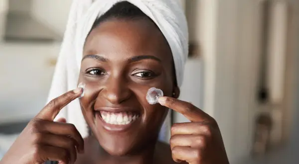Lächelnde Frau mit Handtuch auf dem Kopf trägt Creme auf. Frage: Retinol wie oft?