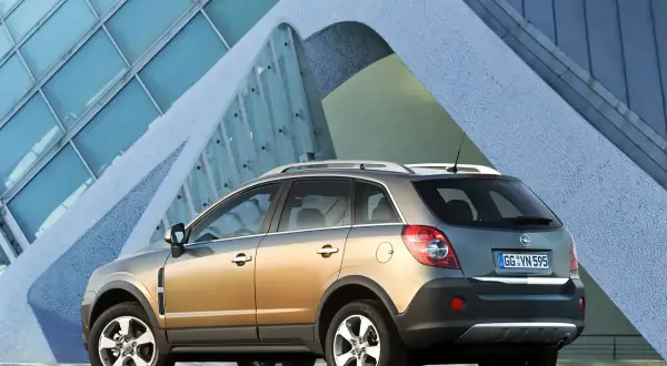 Złoty Opel Antara z nowoczesnym budynkiem w tle.