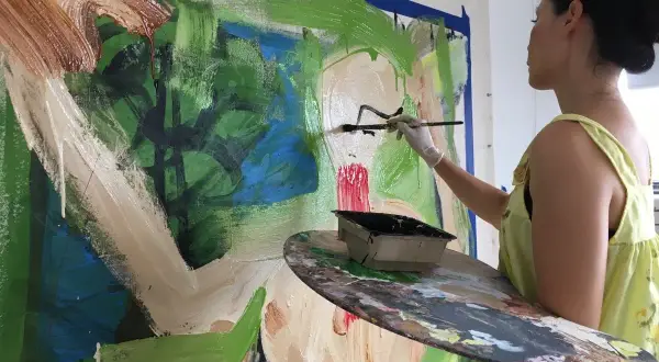 Lucy Liu artwork in progress: the artist adds bold strokes of black paint to a vibrant, abstract canvas, her palette ready for more color.