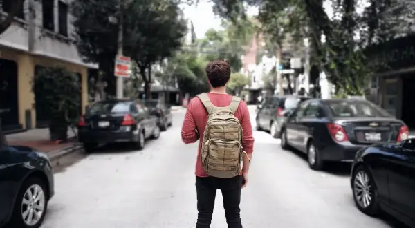Ein junger Mann mit Rucksack steht auf einer Straße in Mittelamerika, bereit für sein nächstes Abenteuer beim Backpacking.