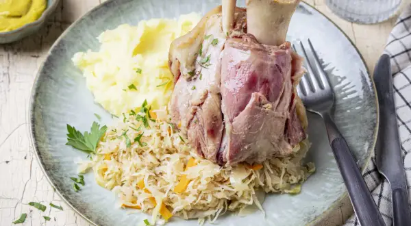 Deftig zubereitetes Eisbein in Sauerkraut kochen, serviert mit Kartoffelpüree und Senf.