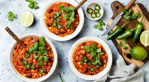 Pyszne chili con carne wege w miseczkach, ozdobione zielonymi listkami i plasterkami jalapeño. Obok limonki i papryczki.