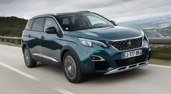 Peugeot 5008 wady i zalety: zielony SUV jedzie po krętej drodze z widokiem na góry.