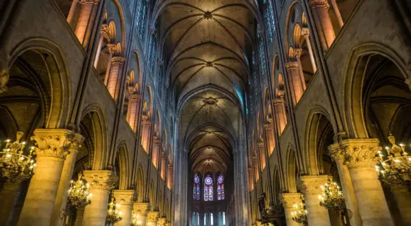 Intérieur de Notre Dame de Paris, avec ses voûtes gothiques, vitraux colorés et chandeliers. On se demande si peut on visiter Notre Dame de Paris.