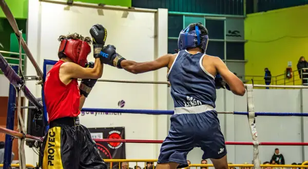 Two young boxers showcase their boxing skills in a ring, one in red, the other in blue, during a match.