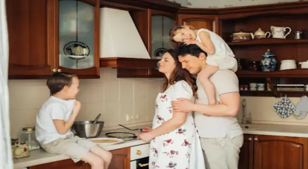 Rodzina w kuchni przygotowuje naleśniki. Tata niesie córkę na barana, mama miesza ciasto, a synek siedzi na blacie. LZO co to? To rodzinne chwile!