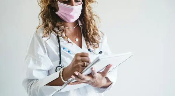 Lekarka w maseczce pisze notatki. Badanie na cito oznacza pilną potrzebę diagnostyki, gdy liczy się każda minuta.