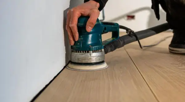 Mano che usa una levigatrice per levigare parquet a mano, creando una superficie liscia e pronta per la finitura.