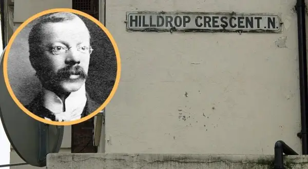 Czarno-białe zdjęcie mężczyzny w okularach i wąsach obok tabliczki z napisem "HILLDROP CRESCENT.N.".