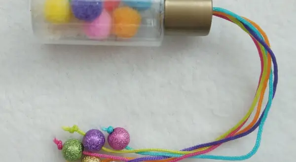 Buntes Rassel-Spielzeug zum selber machen 1 Jahr: Pompons in Fläschchen, bunte Schnüre mit Glitzerkugeln.