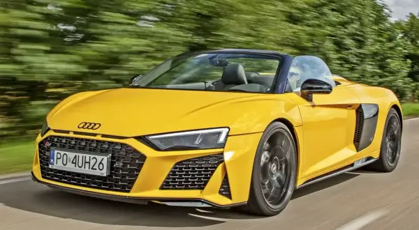 Żółte audi coupe spyder pędzi po drodze, otoczone zielenią drzew.