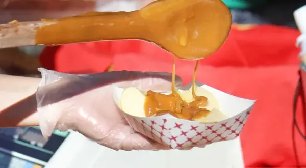 Une cuillère en bois verse du caramel coulant sur des tranches de pomme dans un petit bol. Le caramel est fait avec du sucre, quel sucre pour faire du caramel ?
