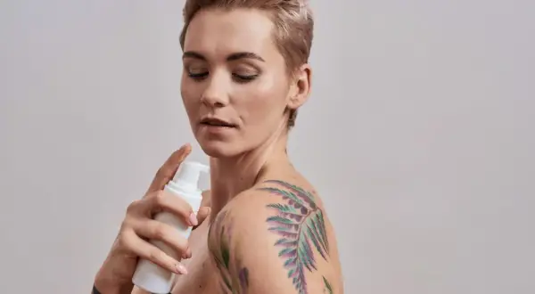 Kobieta z kolorowym tatuażem na ramieniu aplikuje piankę. Dowiedz się, czym myc tatuaz, by zachować jego piękno.