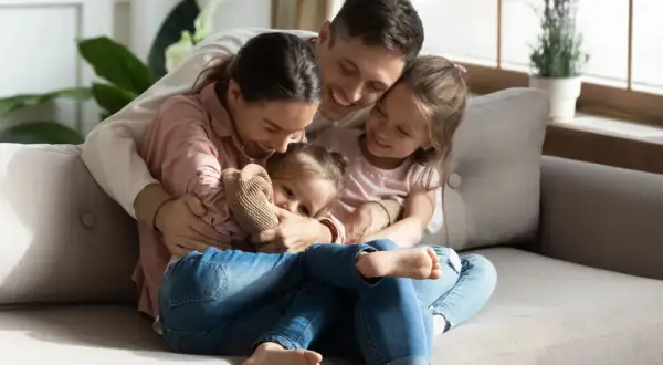 Szczęśliwa rodzina przytula się na kanapie. Nawet po pracy, aktywni rodzice znajdują czas na wspólne chwile z córkami.
