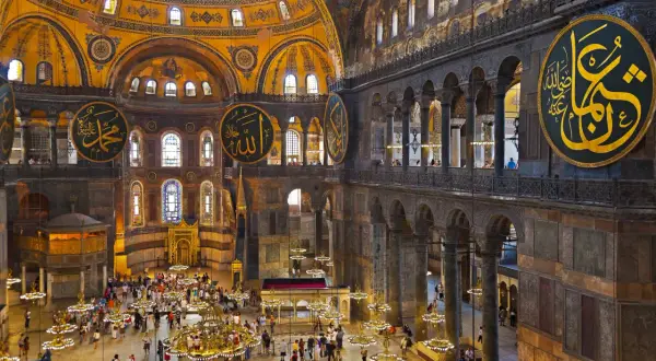 Wnętrze Hagia Sophia z wielkimi okrągłymi kaligrafiami, kopułą i tłumem turystów.