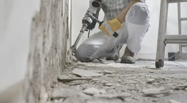 Un ouvrier utilise un marteau-piqueur pour démolir un mur. Des débris jonchent le sol. C'est une étape de travaux, comme dans une lettre d'information.