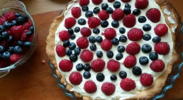 Pyszna tarta na słodko z malinami i borówkami, udekorowana kremem. Idealna na letnie popołudnie.