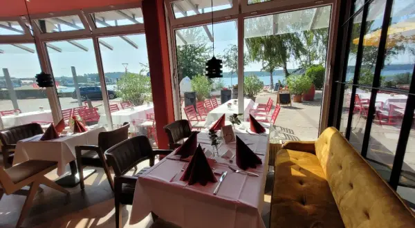 Gemütliche Tische mit rotem Stoff und Blick aufs Wasser – hier könnte das beste Restaurant in Waren sein.