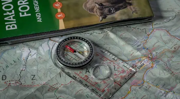 Kompas i mapa pomogą Ci dowiedzieć się, jak używać kompasu w terenie. Widok z góry na sprzęt turystyczny.