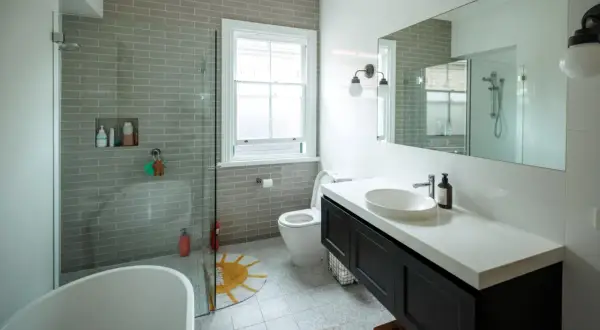 Baño moderno con ducha sin mampara, bañera exenta, lavabo sobre encimera y WC. Azulejos grises y suelo estampado.