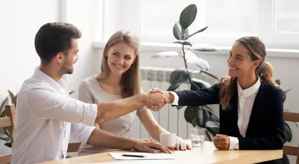 Accordo raggiunto: stretta di mano tra uomo e donna, con una collega sorridente. Si discute di stage e retribuzione minima.