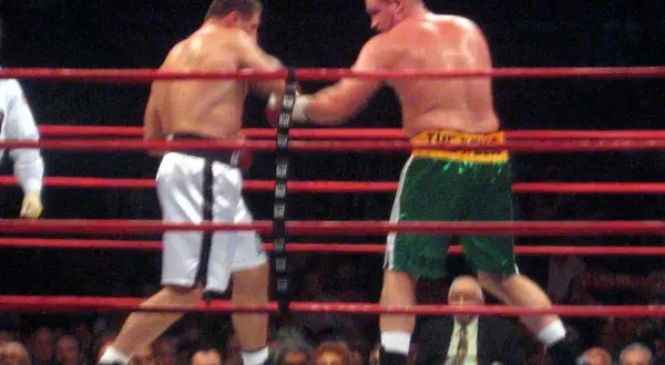 Two boxers in a ring, one in white shorts, the other in green. This bout adheres to the light heavyweight boxing weight limit.