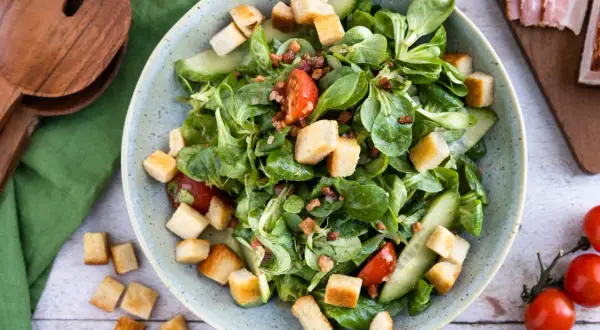 Frischer Feldsalat mit Speck und knusprigen Croutons, garniert mit Tomaten und Gurkenscheiben. Ein Genuss!