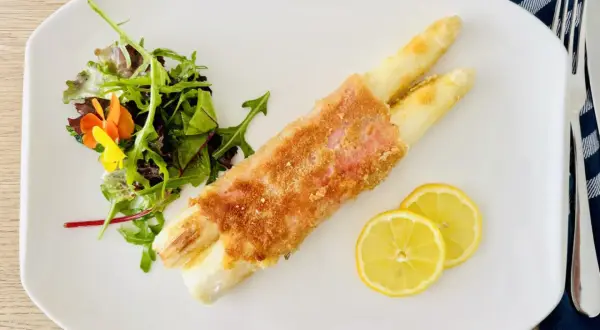 Spargel Cordon Bleu, knusprig paniert, serviert mit frischem Salat und Zitronenscheiben auf einem weißen Teller.