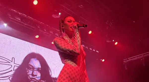 Energetyczny koncert Bambi zdominowany przez czerwone światła. Wokalistka w charakterystycznym stroju z plecionymi włosami śpiewa do mikrofonu.