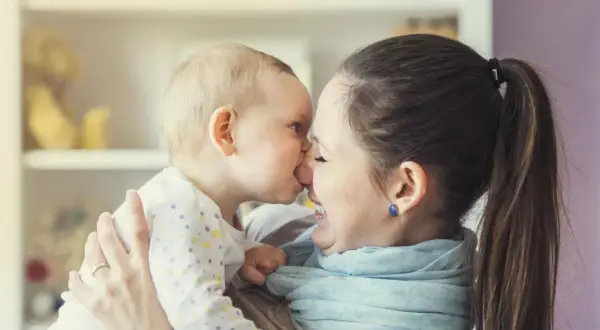 Ein süßer Moment zwischen Mutter und Baby (24 Wochen alt). Das Baby gibt der Mutter einen Nasenkuss, beide lächeln glücklich.